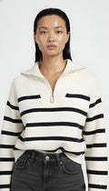 Person wearing a white sweater with black stripes and dark jeans on a white background